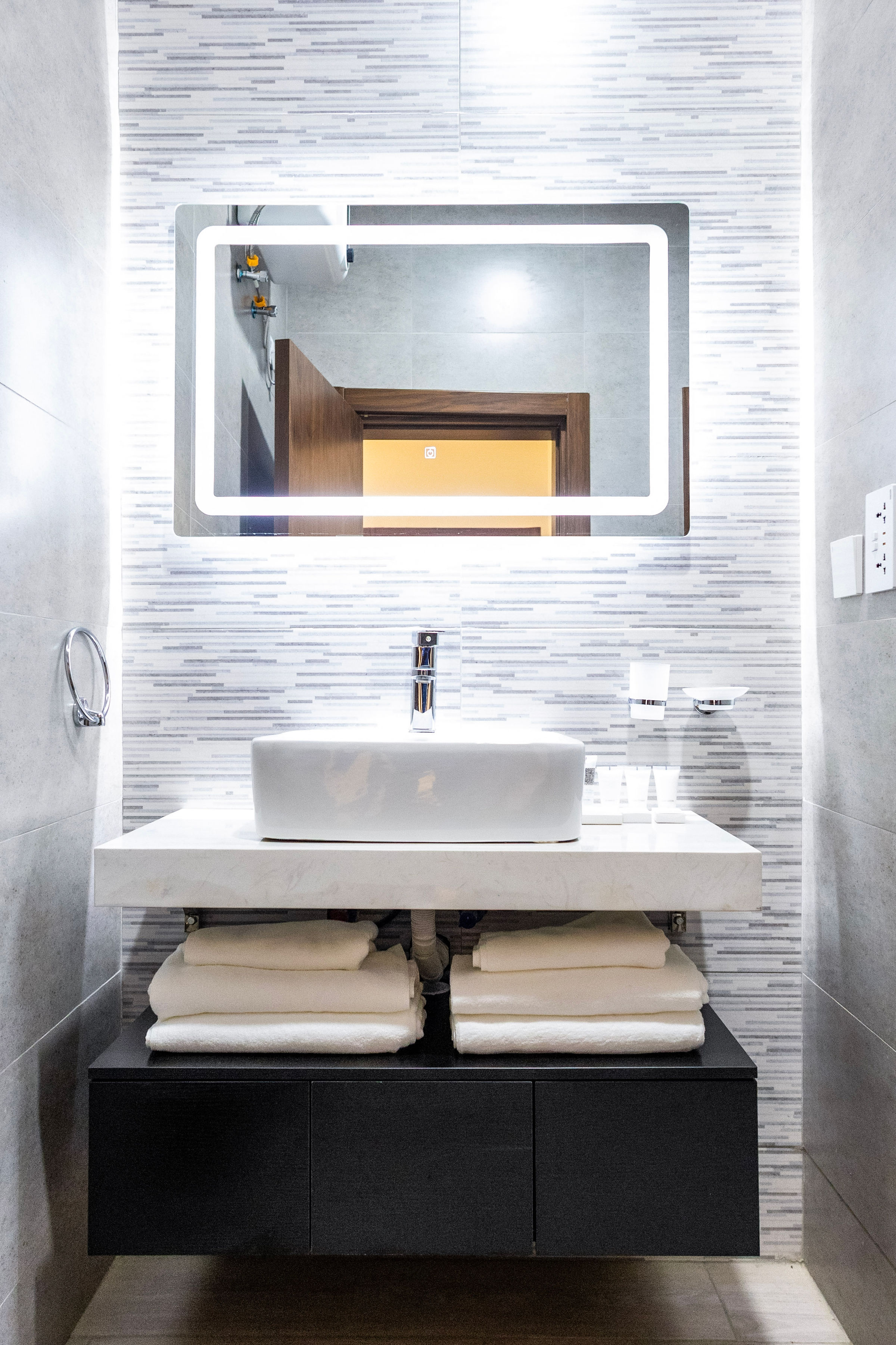 Studio vanity with a vessel basin, backlit mirror and stacked towels
