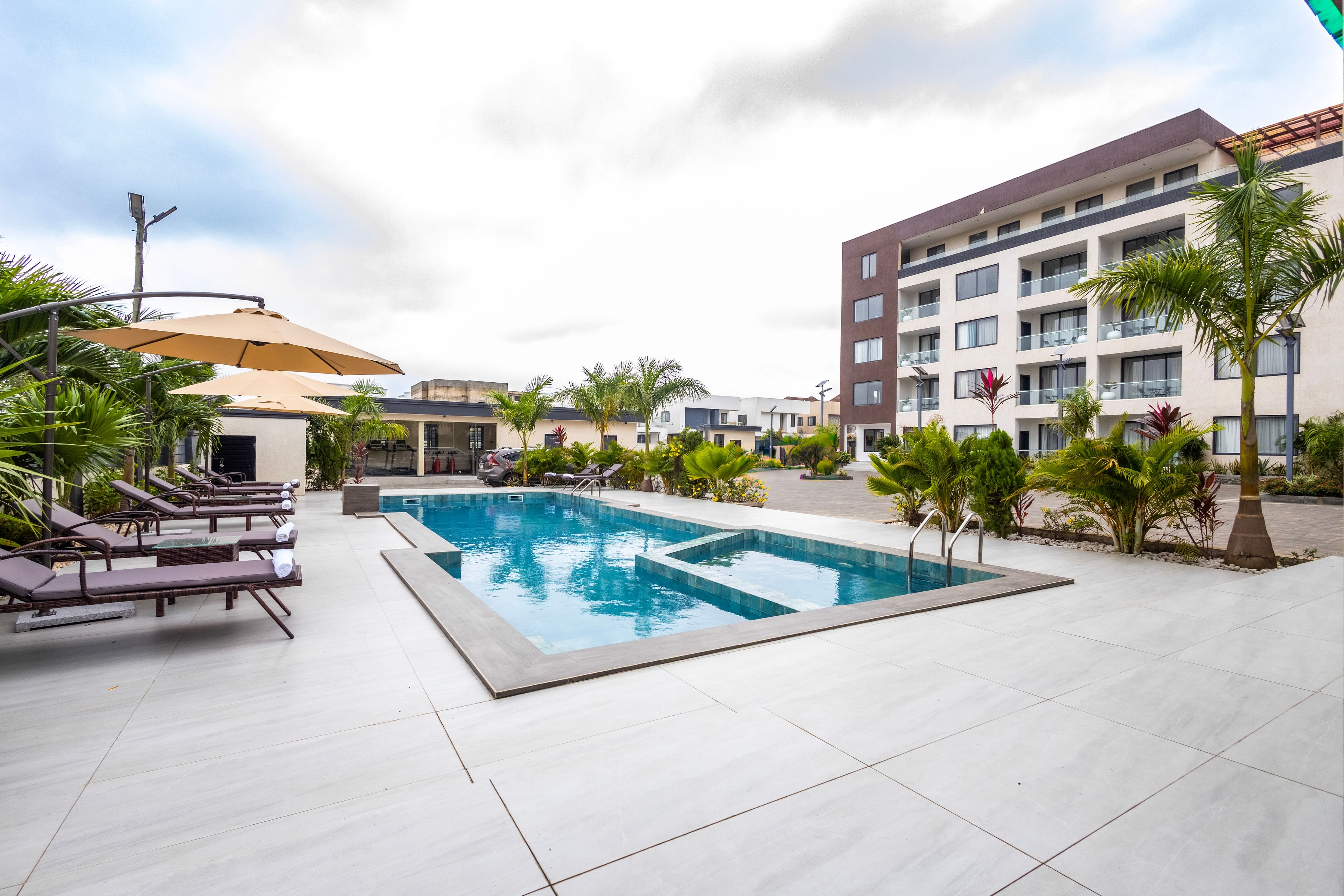 The outdoor pool with sun loungers, palms and the apartments beyond